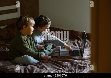 i bambini sono seduti davanti al portatile sul letto per un apprendimento adattivo Foto Stock