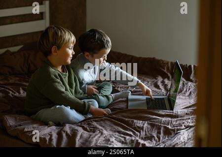 i bambini sono seduti davanti al portatile sul letto per un apprendimento adattivo Foto Stock