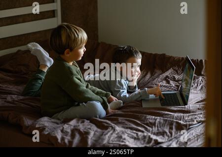 i bambini sono seduti davanti al portatile sul letto per un apprendimento adattivo Foto Stock