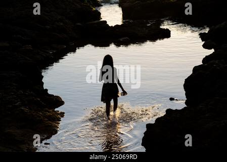 Salvador, Bahia, Brasile - 20 dicembre 2019: Una persona non identificata, in silhouette, che cammina in acqua alla spiaggia di Paciencia, prende il sole. Salvador, Bah Foto Stock