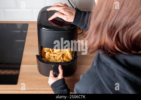 Donna a casa che utilizza un gadget alla moda da cucina, friggitrice, che seleziona un programma su un piccolo forno a convezione sul piano di lavoro per friggere in profondità senza olio, salutare W Foto Stock