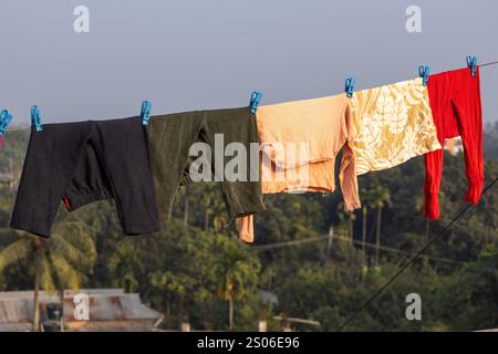 I vestiti bagnati per bambini sono appesi su una linea di abbigliamento sul tetto di un edificio, asciugando al sole e al vento. Foto Stock