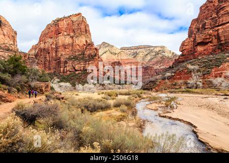 Un gruppo di persone sta camminando lungo un fiume in un deserto. Il paesaggio è arido e roccioso, con pochi alberi sparsi intorno. Il cielo è nuvoloso, e.. Foto Stock