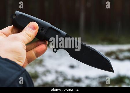 Coltello tattico a lama fissa nella mano di un uomo in una foresta invernale. Foto Stock