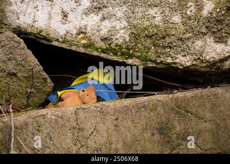 Orsacchiotto marrone per bambini e bandiera Ucraina sotto le macerie in Ucraina, guerra Foto Stock