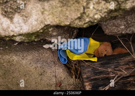 Orsacchiotto marrone per bambini e bandiera Ucraina sotto le macerie in Ucraina, guerra Foto Stock