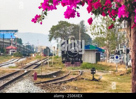 Alla stazione ferroviaria di Hua Hin, piante sospese che mostrano una bella e vibrante fioritura, con la luce del tardo pomeriggio, incorniciano una locomotiva a vapore d'epoca in disuso Foto Stock