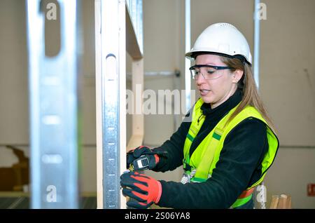 Lavoratore edile che esegue misurazioni di cartongesso utilizzando un misuratore di distanza laser, garantendo un'installazione precisa durante il processo di costruzione Foto Stock