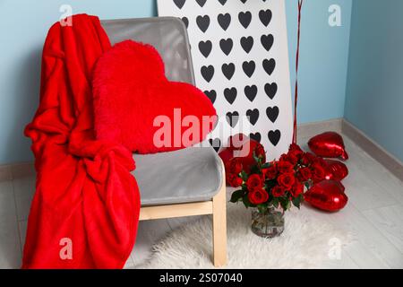 Comoda sedia con palloncini a forma di cuore, bouquet di rose e confezione regalo vicino alla parete blu Foto Stock