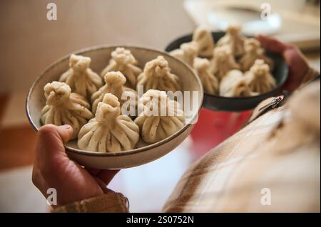 Primo piano di una persona con due piatti pieni di gnocchi tradizionali georgiani appena fatti, o Khinkali, esposti in un'accogliente atmosfera da cucina. Rif Foto Stock
