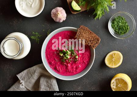 Zuppa di crema di barbabietole con yogurt, cetrioli e aneto nel recipiente su sfondo scuro. Zuppa fredda estiva. Vista dall'alto, disposizione piatta Foto Stock