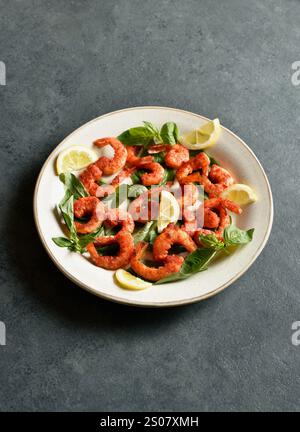 Gamberi speziati al basilico tailandese su piatto su sfondo blu. Vista ravvicinata Foto Stock