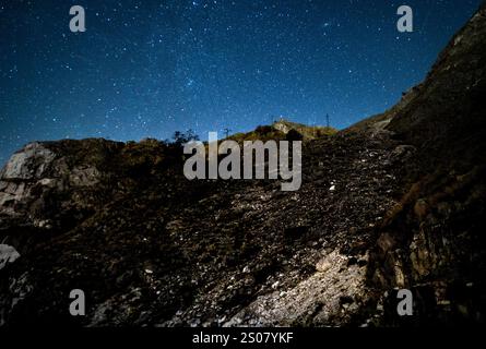 Una collina rocciosa sotto un cielo stellato, che mostra una vista chiara di numerose stelle e un pizzico di vegetazione. Il paesaggio è illuminato da moonlig Foto Stock