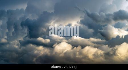 Cielo spettacolare pieno di nuvole scure e vorticose, illuminato da una luce soffusa che sbircia. Le nuvole creano un'atmosfera soffusa, suggerendo un'impendi Foto Stock