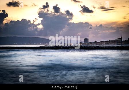 Una tranquilla scena costiera al crepuscolo, caratterizzata da dolci onde che si infrangono su una costa rocciosa. Il cielo è pieno di nuvole spettacolari illuminate dalla dissolvenza Foto Stock