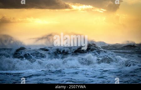 Un paesaggio marino spettacolare caratterizzato da onde turbolente che si infrangono l'una contro l'altra sotto un cielo dorato al tramonto. L'oceano è pieno di creme di whitecaps, create Foto Stock