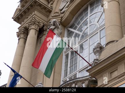 Un primo piano della bandiera ungherese che sventola accanto a una bandiera dell'Unione europea su un edificio storico di Budapest. Foto Stock