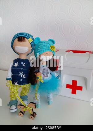 Due bambole fatte a mano indossano maschere protettive e stanno in piedi vicino a un kit di pronto soccorso, promuovendo la sicurezza e la salute Foto Stock