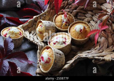 I muffin al mirtillo appena sfornati si trovano in un cesto di vimini, circondati da vivaci foglie autunnali, creando un ambiente accogliente e invitante Foto Stock