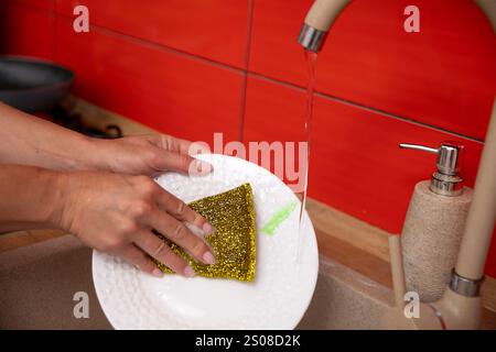 Lavare i piatti sporchi nel lavandino della cucina con una spugna per strofinarli e pulirli accuratamente Foto Stock