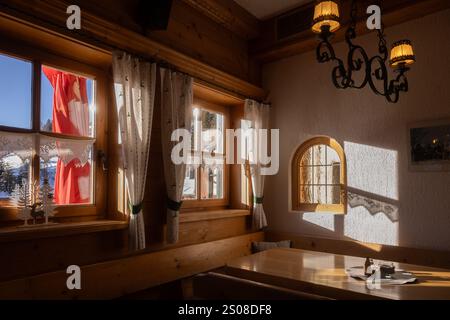 Intimo interno di un rifugio di montagna con luce del sole che scorre attraverso finestre di legno in un ambiente invernale Foto Stock