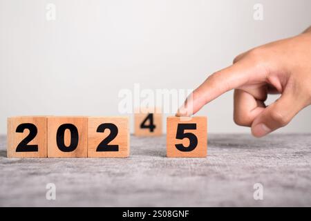 Una mano sostituisce 2024 con 2025 utilizzando blocchi cubici di legno. Pianificazione aziendale e conto alla rovescia fino al 2025 Foto Stock