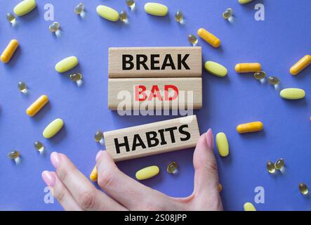 Infrangere il simbolo delle cattive abitudini. Le parole concettuali rompono le cattive abitudini sui blocchi di legno. Bellissimo sfondo viola con pillole. Mano del dottore. Medicine e Break Bad Foto Stock