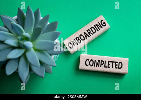 Simbolo onboarding completato. Termine concettuale onboarding completato su blocchi di legno. Splendido sfondo verde con piante succulente. Business e a bordo Foto Stock