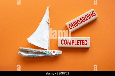 Simbolo onboarding completato. Termine concettuale onboarding completato su blocchi di legno. Bellissimo sfondo arancione con barca. Business and Onboarding Comple Foto Stock