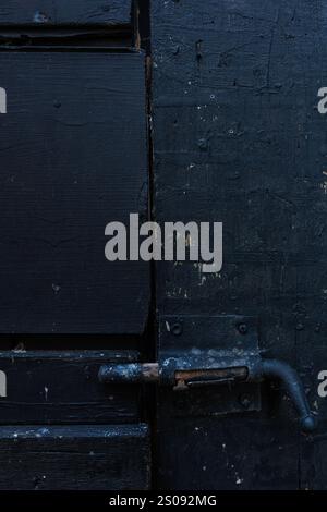 Dettaglio di una piccola porta nera con serratura arrugginita. La porta è fatta di legno Foto Stock