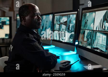 Guardia di sicurezza maschile matura che si concentra sulla visione di video cctv sullo schermo di un computer desktop mentre è seduto sul posto di lavoro Foto Stock