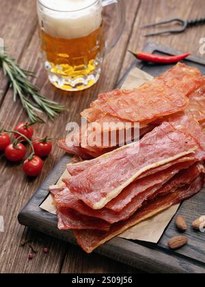 Maiale affumicato e patatine di pollo su un vassoio di legno con verdure e un bicchiere di birra leggera sul tavolo Foto Stock