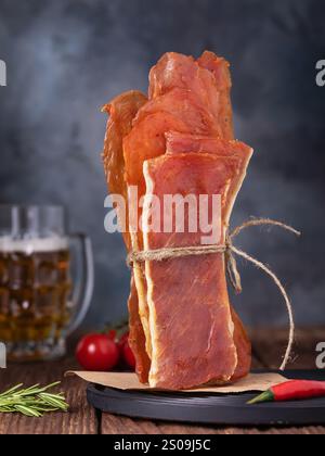 Maiale affumicato, pollo e patatine di tacchino su banco in ceramica con verdure e spezie sul tavolo, spuntino con birra fresca Foto Stock