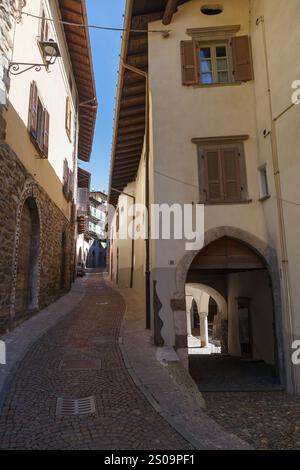 Vista sulla strada del villaggio storico di Gromo, Bergamo, Lombardia, Italia. Stradine acciottolate strette. Luci e ombre solari. Foto Stock