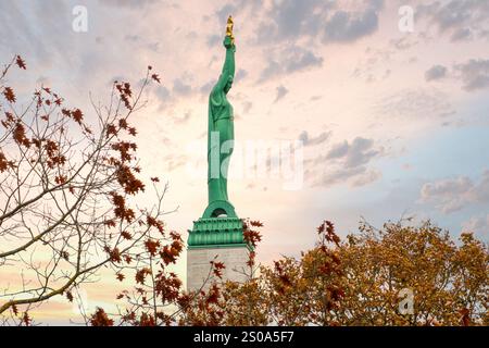 Il Monumento alla libertà si erge alto a riga, in Lettonia, con stelle che tengono la libertà. Alberi autunnali con foglie marroni rossastre circondano la base sotto una pasta Foto Stock