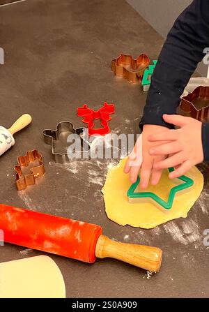 Primo piano di un bambino che prepara biscotti natalizi con un impasto sul tavolo della cucina Foto Stock