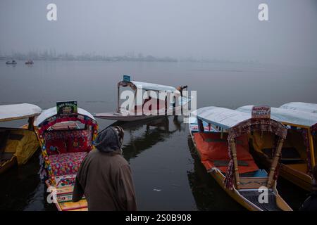 Srinagar, Jammu e Kashmir, India. 27 dicembre 2024. Un uomo usa un reo per rompere le acque parzialmente congelate del lago dal in una fredda mattina invernale a Srinagar. Il periodo di 40 giorni di freddo invernale estremo, noto come ''˜Chillai Kalan', ' è iniziato con piena furia il 21 dicembre e terminerà il 30 gennaio. (Immagine di credito: © Adil Abass/ZUMA Press Wire) SOLO PER USO EDITORIALE! Non per USO commerciale! Foto Stock