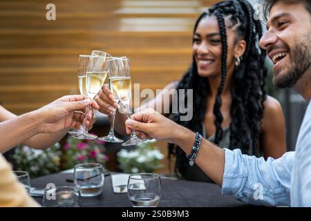 Un gruppo gioioso di amici brindando con bicchieri di champagne a una cena all'aperto, condividendo risate e festeggiando insieme in un'atmosfera vivace Foto Stock