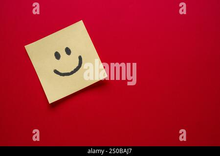 Emoji Smiley Face disegnando su carta adesiva su sfondo rosso Foto Stock