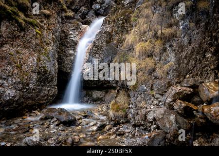 Una cascata serena scende lungo una scogliera rocciosa circondata da muschio e vegetazione. Foto Stock