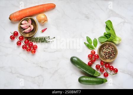 Le verdure fresche dai colori vivaci, tra cui carote, zucchine e pomodori, sono disposte artisticamente su una superficie in marmo, pronte per la cottura. Erbe An Foto Stock