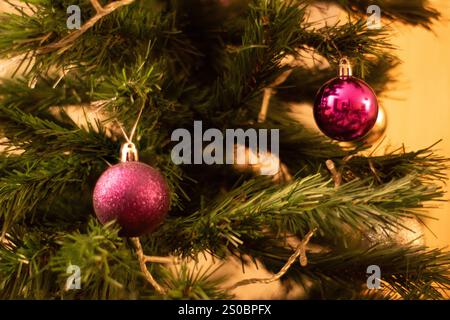 Foto ravvicinate di ornamenti per alberi di Natale con baule dorate, viola e rosa che si illuminano sotto una luce calda. Le decorazioni natalizie creano un ambiente accogliente e accogliente Foto Stock