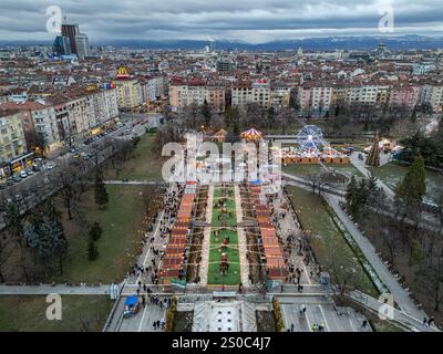 Una vibrante vista aerea del mercato di Natale di Sofia vicino al Palazzo Nazionale della Cultura (NDK). Luci festive, ruota panoramica e fascino invernale. Foto Stock