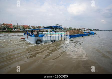 Mekong Delta, Vietnam. 27 dicembre 2024: Nave da carico/chiatta carica di vele di sabbia sul famoso corso d'acqua. L'estrazione di sabbia e ghiaia (miniere o draghe) utilizzata per il calcestruzzo nell'industria edile solleva avvertenze circa l'impatto ambientale del sovrasfruttamento dei sedimenti del letto dei fiumi (biodiversità ed ecosistema), ma anche sulla vita delle persone che vivono sulle rive dei fiumi. Lo sfruttamento legale o illegale della sabbia provoca una massiccia erosione delle banche, con conseguente perdita di terreni agricoli, ma anche il crollo di edifici e case e lo spostamento delle popolazioni. Crediti: KEVIN IZORCE/Alamy Live News Foto Stock