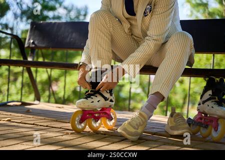 Primo piano di un uomo in tuta a strisce che regola i pattini a rotelle mentre è seduto sulla panchina del parco Foto Stock