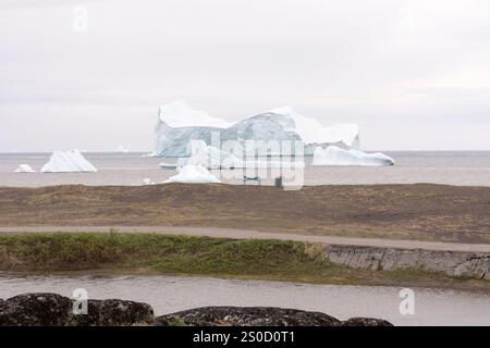 Questa tranquilla immagine cattura una tranquilla spiaggia in Groenlandia, con una panchina solitaria che si affaccia sul vasto oceano e gli iceberg torreggianti. La calma, l'ampia Foto Stock