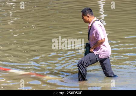 SAMUT PRAKAN, TAILANDIA, 19 novembre 2024, Un uomo aspetta attraverso una strada allagata Foto Stock