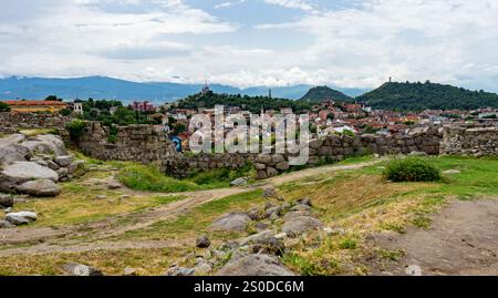 Antiche rovine di pietra che si affacciano su una città con colline sullo sfondo. Foto Stock