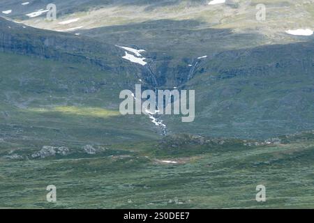 Splendido paesaggio con una cascata nelle montagne norvegesi e un ampio campo verde in primo piano. Foto Stock
