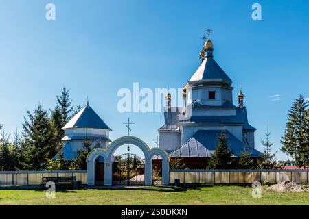 Una grande chiesa con un tetto bianco e un cielo blu sullo sfondo. La chiesa è circondata da alberi e da una recinzione Foto Stock